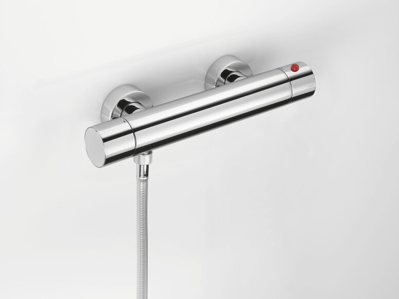 HEWI Fittings AQ Shower Thermostat Chrome-plated thermostat with a red knob and a hose connection on the lower left-hand side of a white wall