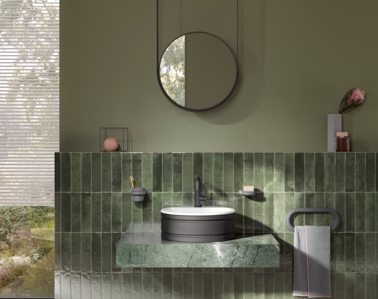 A round washbasin set on a green marble vanity unit with a black tap and towel holder, with a round mirror above it