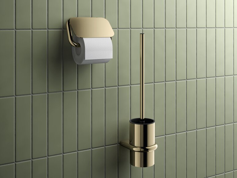 HEWI Range 480 PVD toilet brush unit and toilet roll holder Toilet brush with a brass-coloured PVD coating and a matching toilet roll holder against a backdrop of green tiles