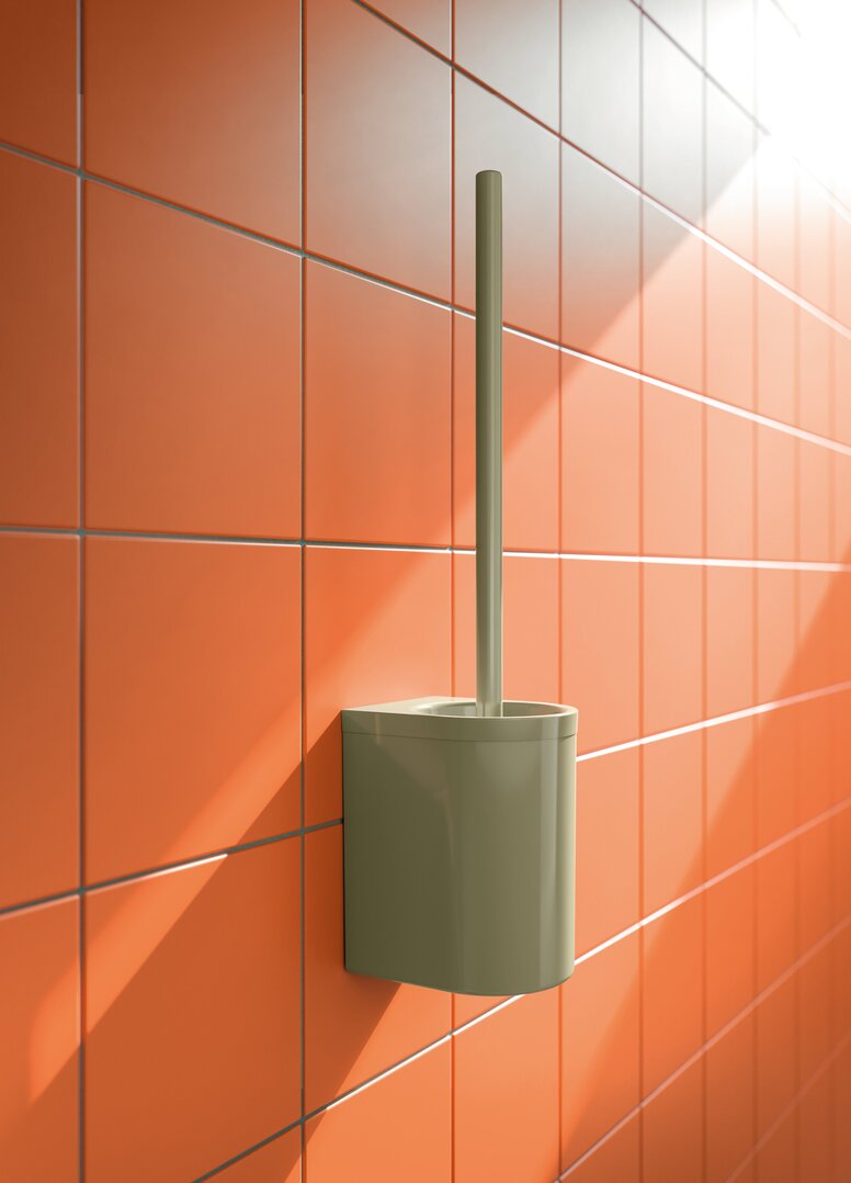 HEWI System 700 toilet brush unit Green wall-mounted plastic toilet brush unit with a long handle and a rectangular container with rounded corners on an orange tiled wall