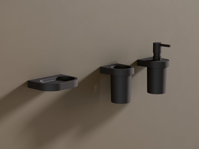 HEWI System 800 shelf, tumbler, soap or disinfectant dispenser A black powder-coated soap dish, along with a tumbler and a soap dispenser, against a brown wall