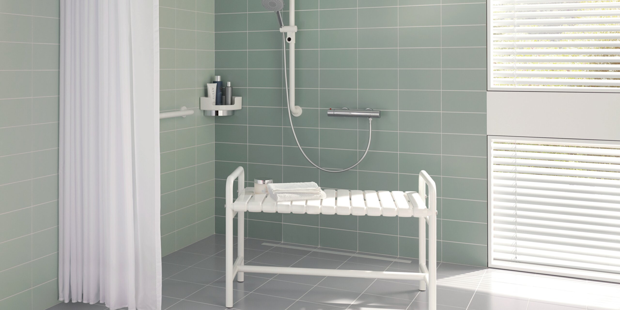 White shower bench with armrests and a shelf in the shower area against a light green tiled wall