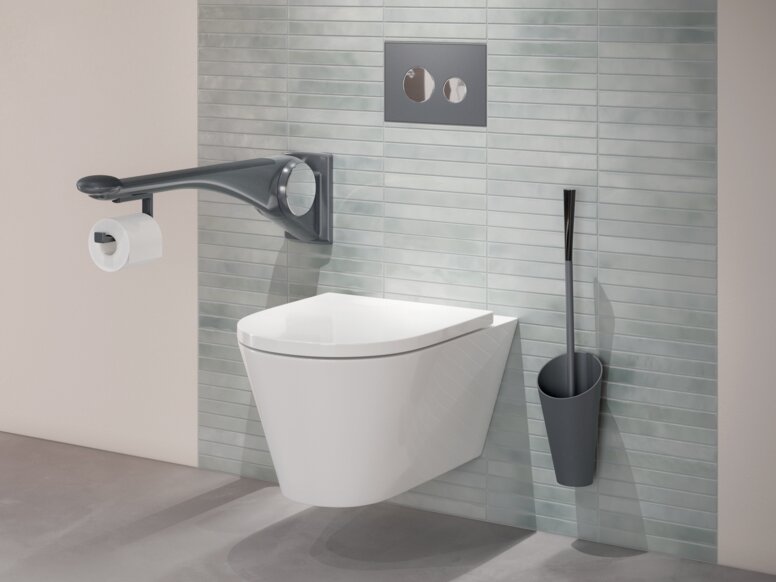 Wall-hung WC with a side support rail, an integrated toilet roll holder and a toilet brush mounted on a green tiled wall