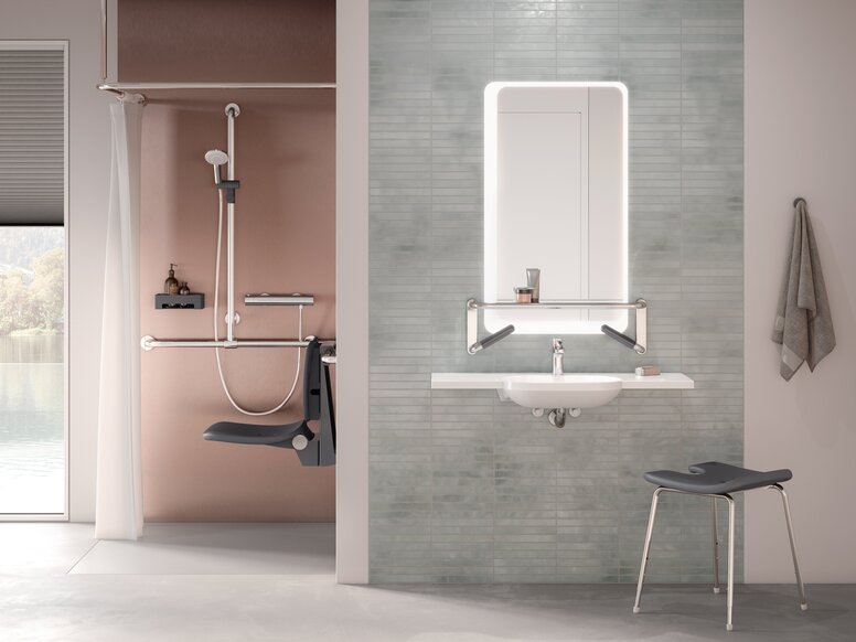A shower seat and handrail attached to a rail with shower head holder in a shower area, next to which is a washbasin mounted on a tiled wall