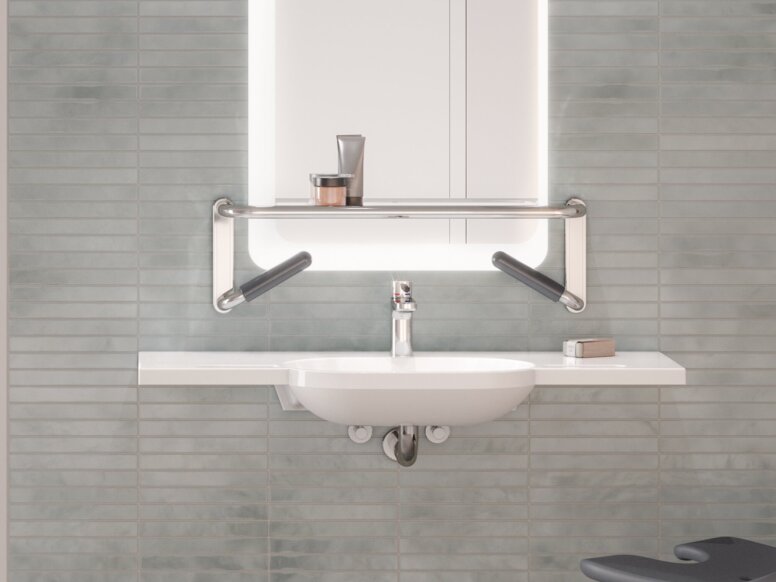 A shower seat and handrail attached to a rail with shower head holder in a shower area, next to which is a washbasin mounted on a tiled wall