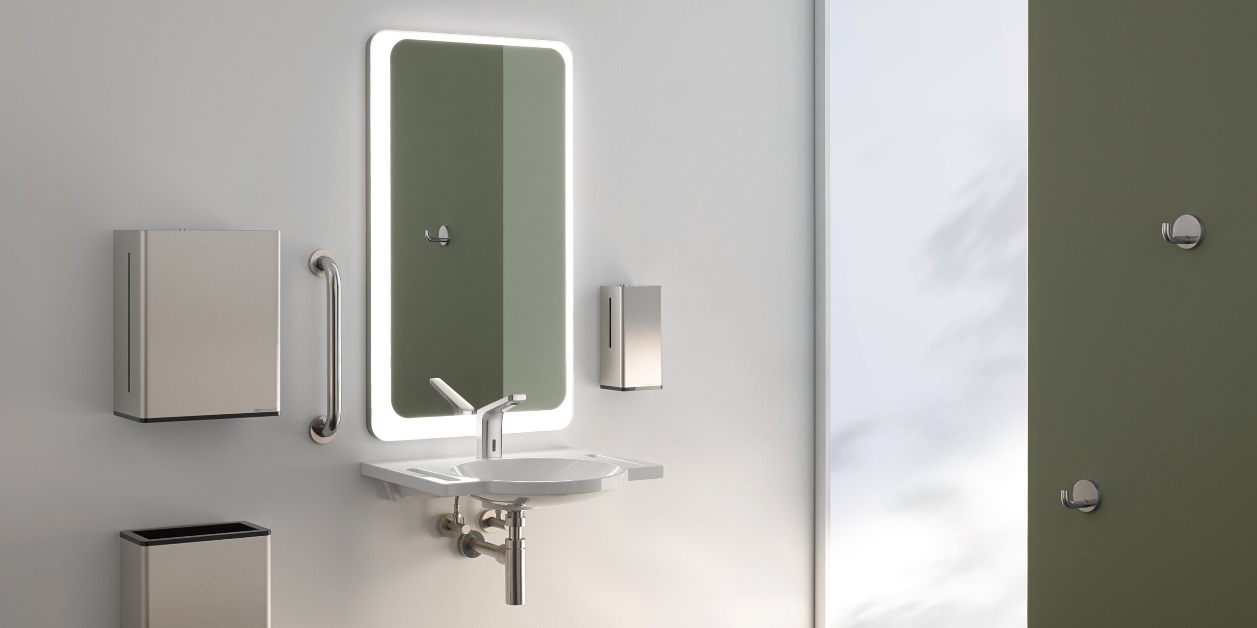 A lighted mirror, with a washbasin underneath, complete with a paper towel dispenser and a waste bin, against a white wall