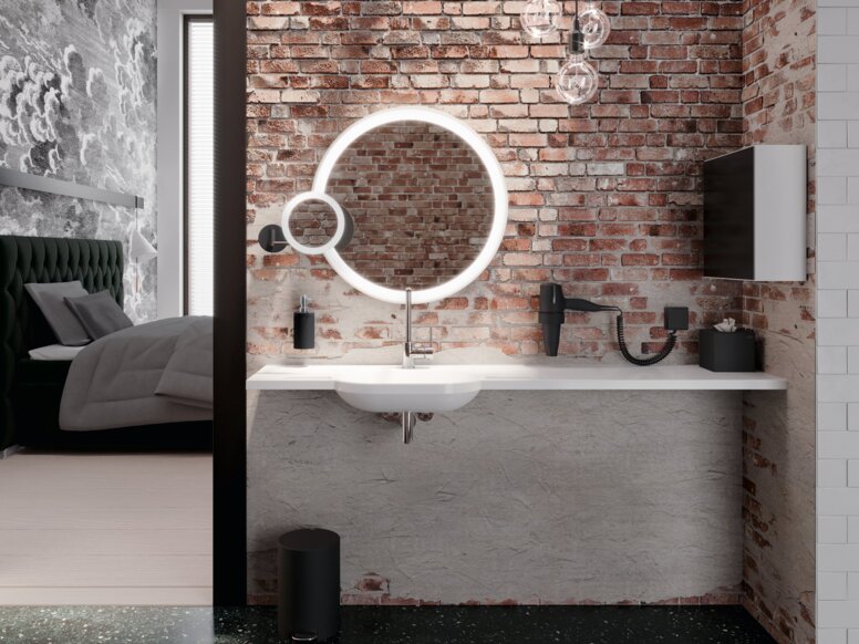 Illuminated wall mirror, make-up mirror and soap dispenser next to a white washbasin with a long shelf and tap
