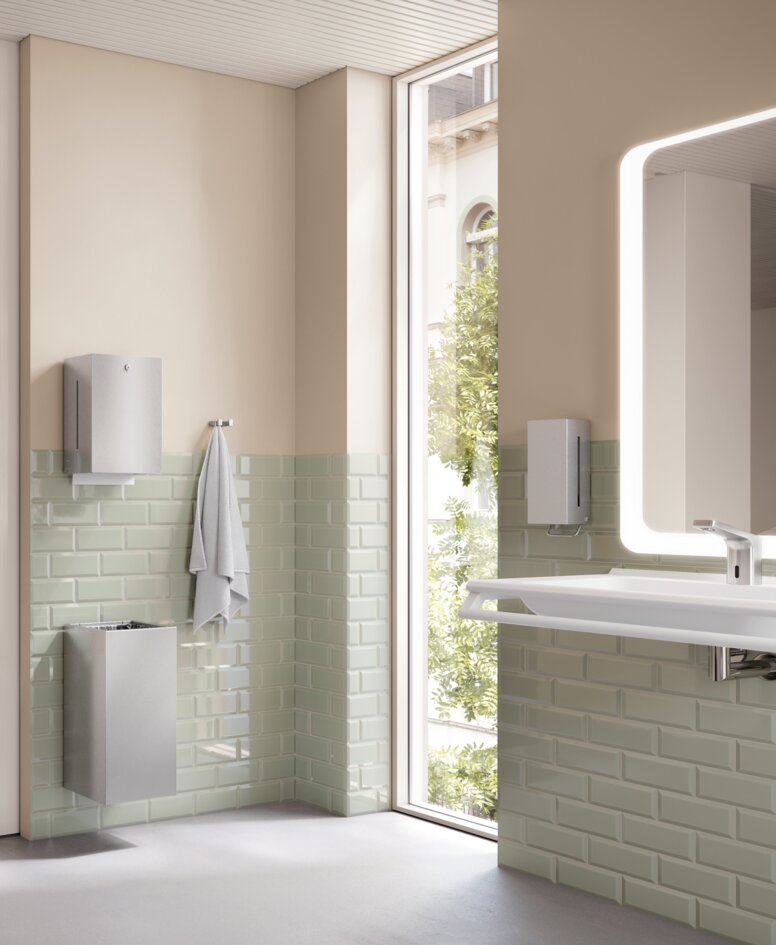 WC with toilet roll holder, support rail and toilet brush in a bathroom with light green tiles and a beige-coloured wall