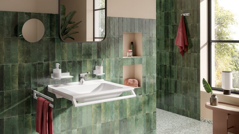 A white washbasin with a tap and a support rail, as well as a soap dispenser and a towel holder, set against a green tiled wall