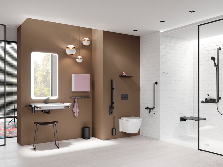 HEWI System 900 Bathroom Interior Modern bathroom with a wall-hung toilet against a brown feature wall, a washbasin with an illuminated mirror and stool on the left, and a level-access shower with a glass partition and dark grab rails on the right